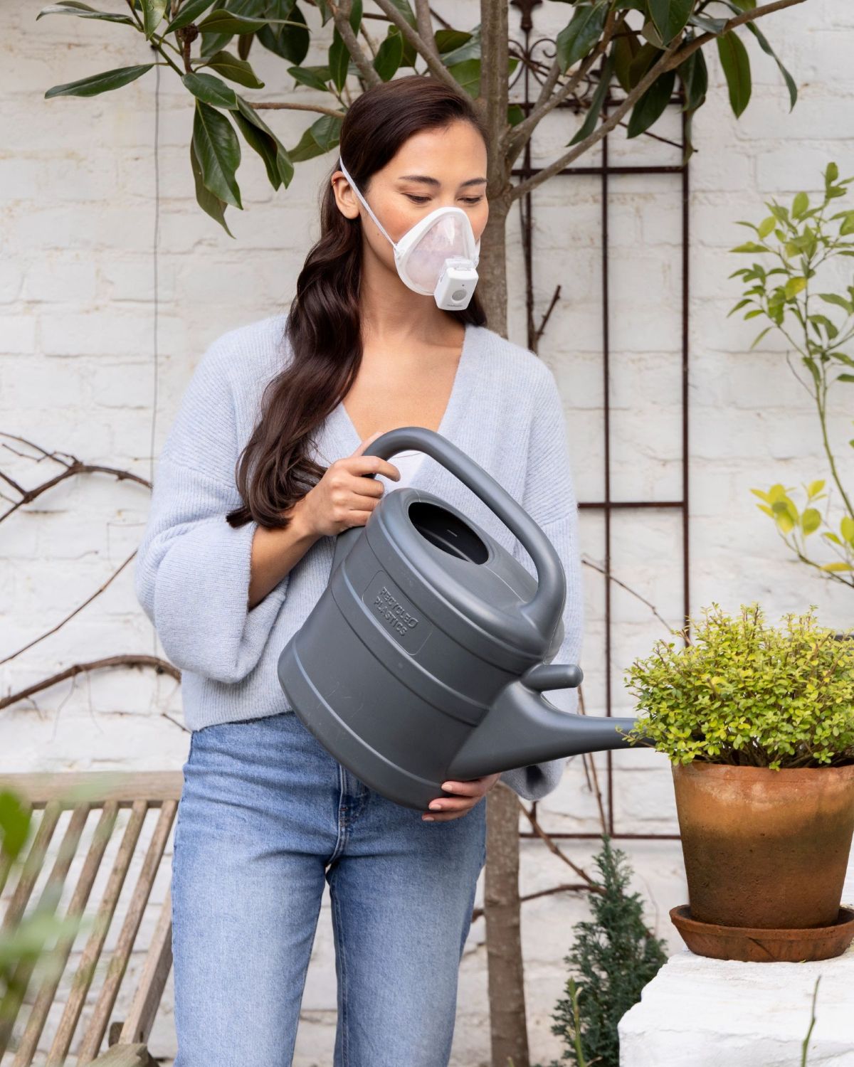 Frau trägt Medisana IN 700 Inhalator mit Maske beim Gießen der Pflanzen – mobile Inhalationstherapie für mehr Freiheit im Alltag